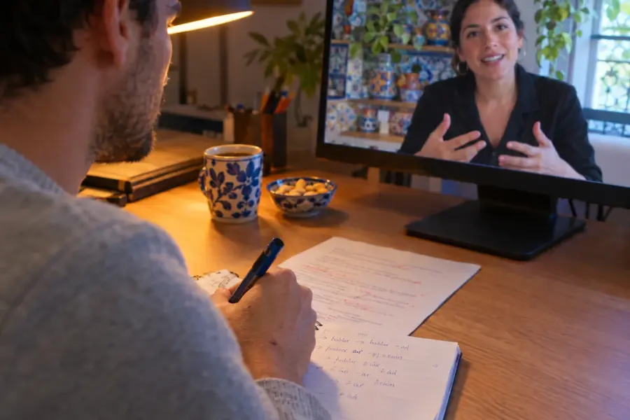 Learner taking notes during a Spanish video lesson with a native teacher